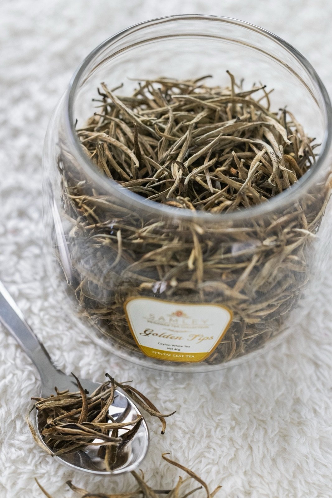Macro of loose golden tea leaves in a glass jar with a spoonful